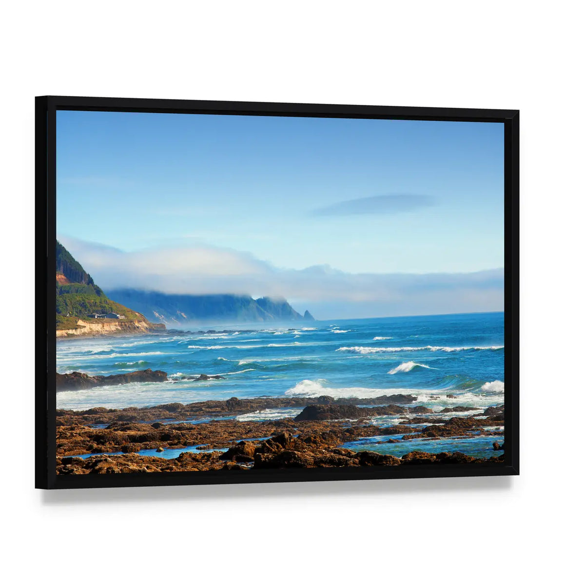 Rocky Shoreline with Crashing Waves and Misty Coastal Hills Canvas Wall Art, framed canvas in a black floater frame, angled product view