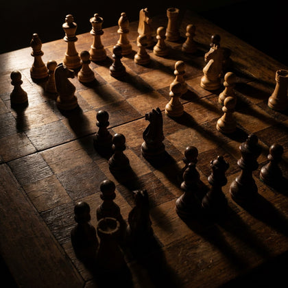 Chess Wall Art canvas print, a chess board mid game, carved wooden pieces casting long shadows under a single raking light