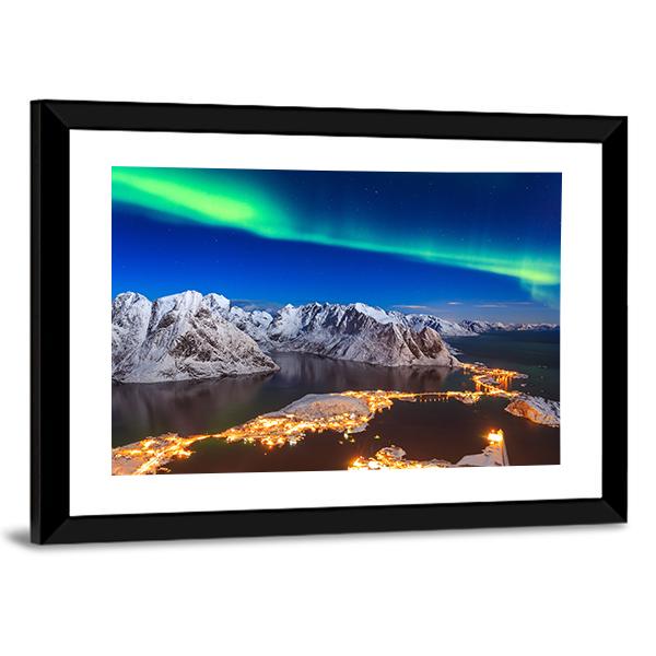 Aurora Over Snowy Mountain Village Canvas Wall Art in white, green and blue, hung on a wall