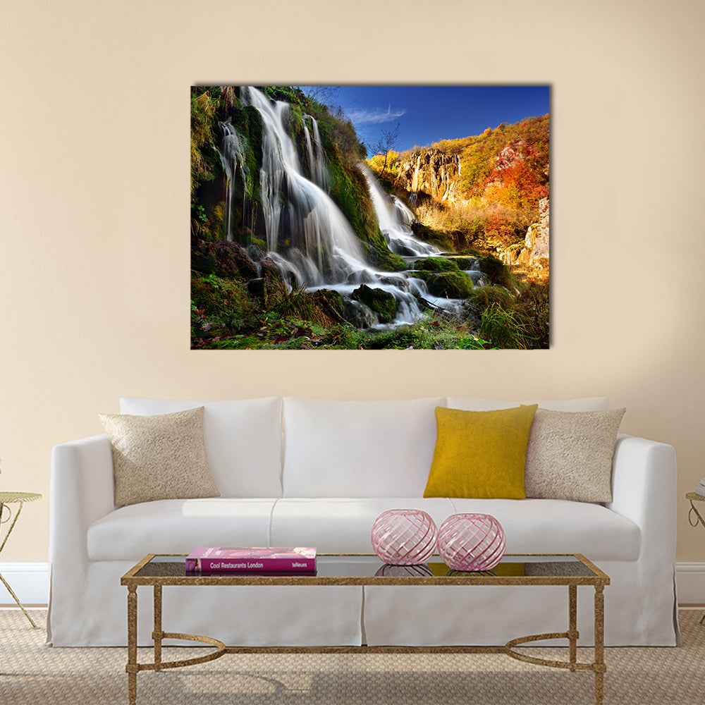 Autumn Waterfall with Mossy Rocks Canvas Wall Art in brown, orange and green, single panel hung on a wall