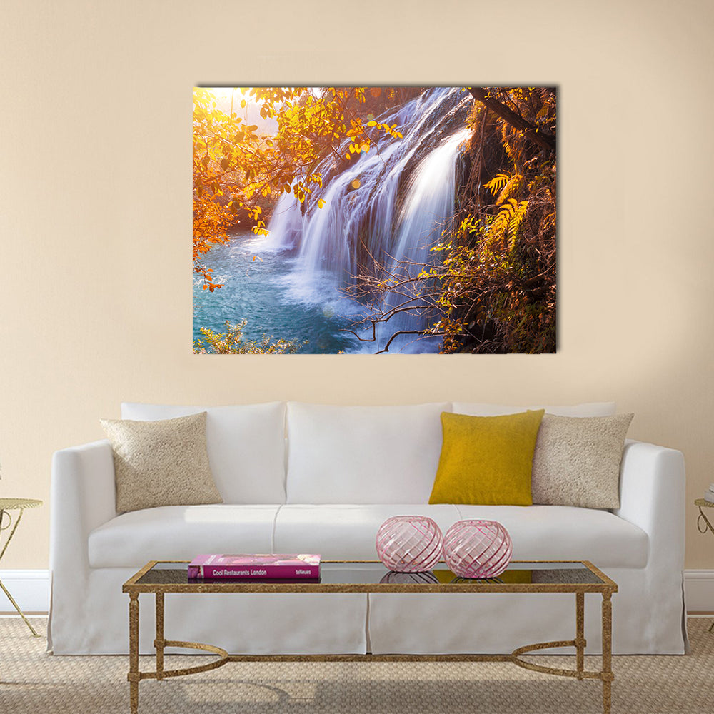 Autumn Waterfall with Sunlit Foliage Canvas Wall Art in orange, yellow and blue, single panel hung on a wall