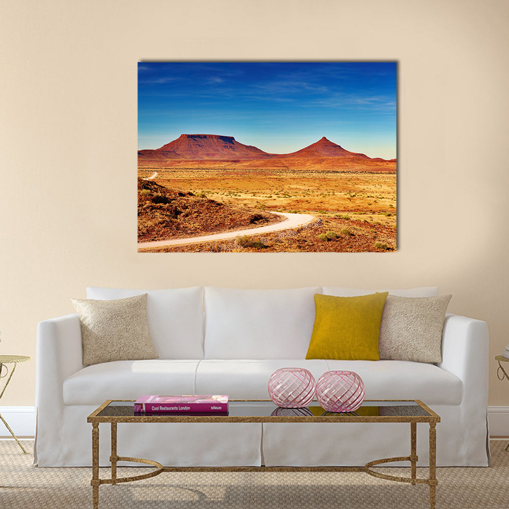 Winding Desert Road to Distant Peaks Canvas Wall Art in brown, orange and blue, single panel hung on a wall
