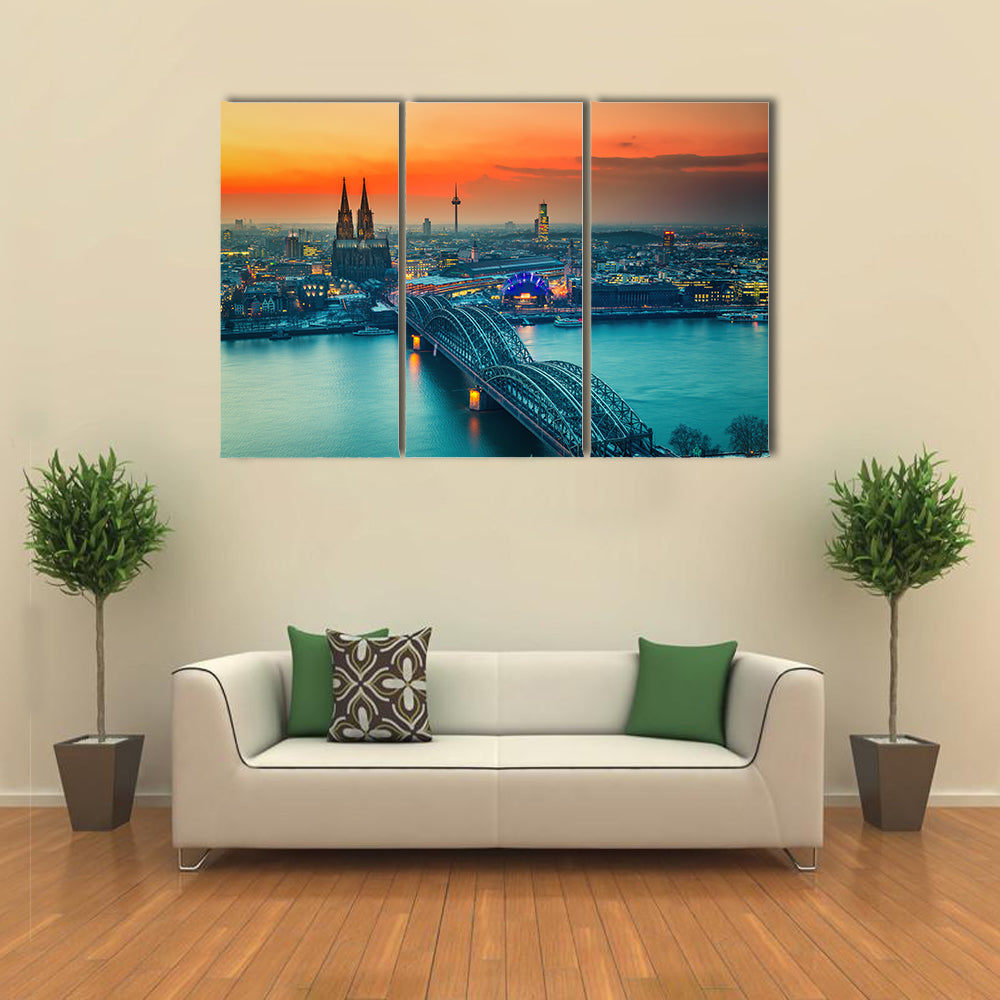 Cologne Cathedral And Hohenzollern Bridge At Night In Germany Canvas Wall Art in gray, orange and yellow, 3 panel horizontal set hung on a wall
