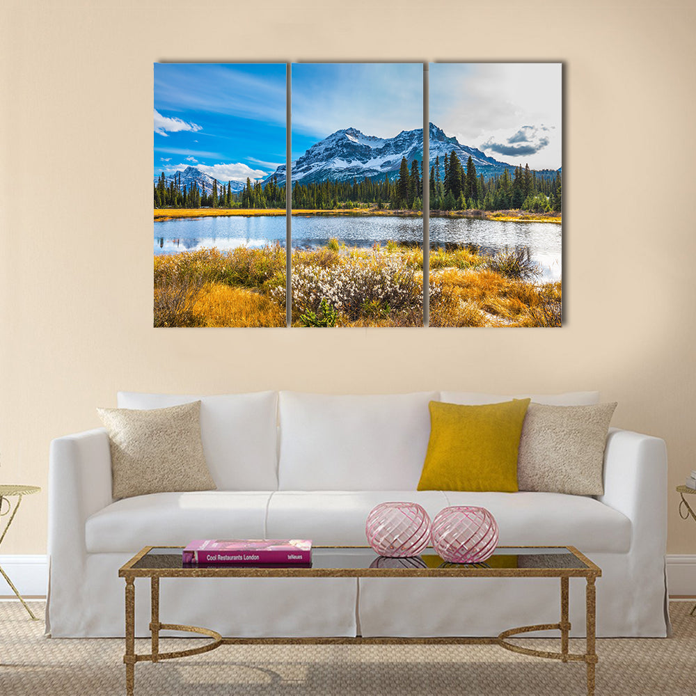 Snowy Rocky Mountains Lake Reflection Canvas Wall Art in yellow, green and blue, 3 panel horizontal set hung on a wall