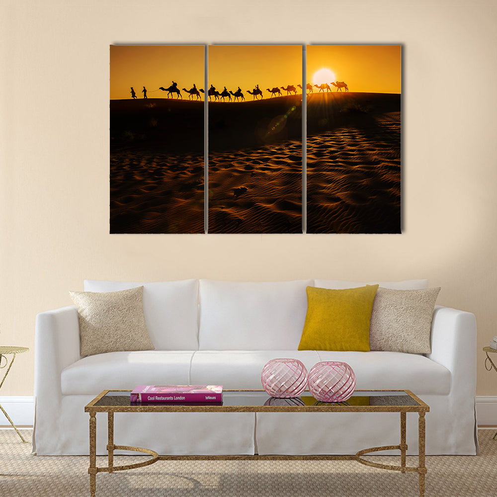 Camel Caravan at Sunset Canvas Wall Art in black, orange and yellow, 3 panel horizontal set hung on a wall