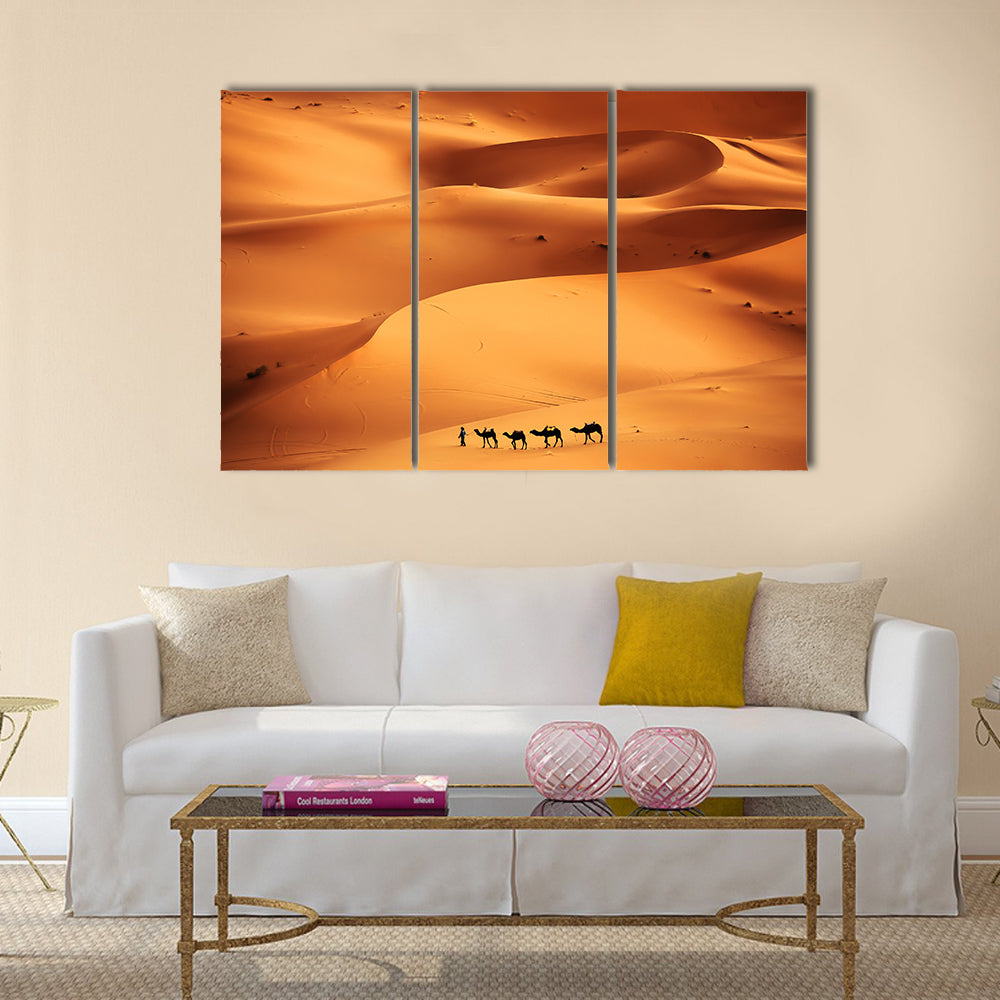 Camel Caravan Across Sahara Sand Dunes Canvas Wall Art in brown, orange and yellow, 3 panel horizontal set hung on a wall
