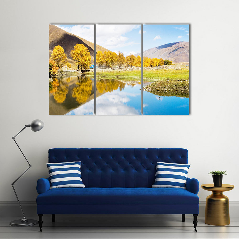 Autumn Mountain Lake with Golden Trees Canvas Wall Art in gold, yellow and blue, 3 panel horizontal set hung on a wall