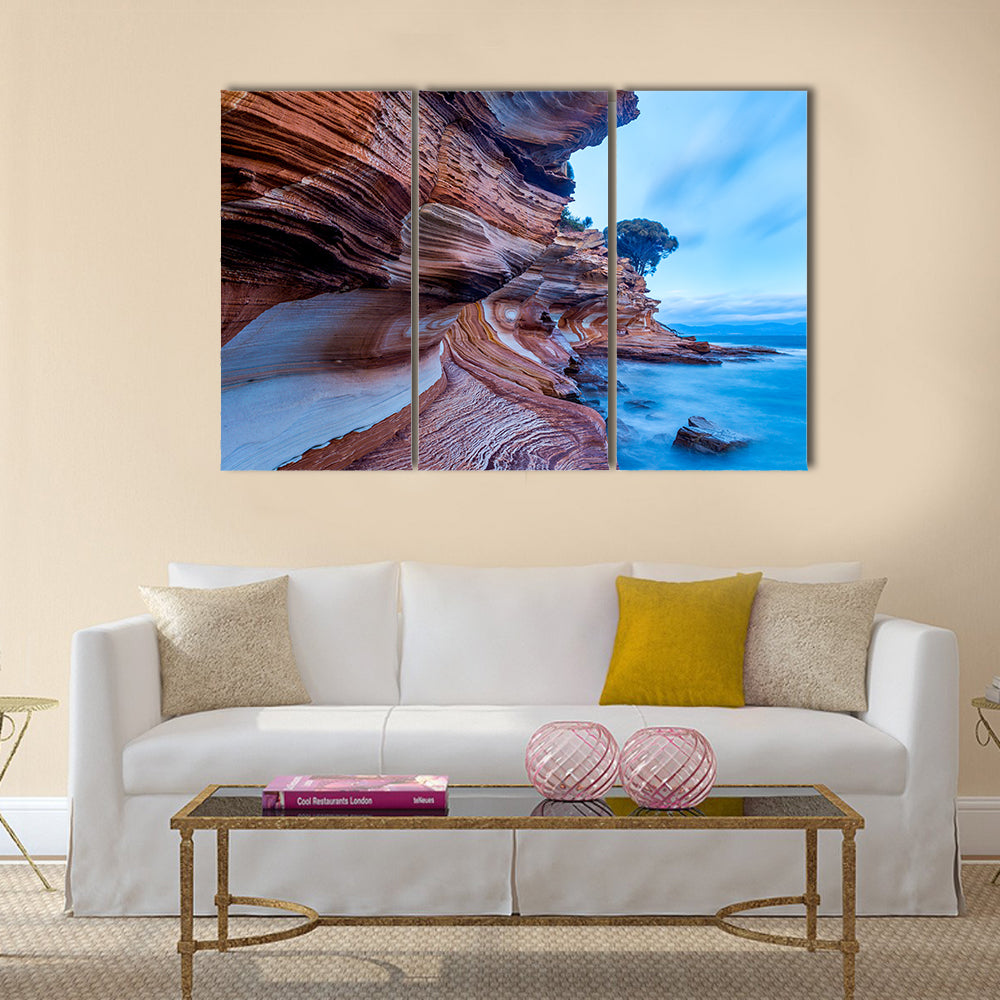 Painted Cliffs on Maria Island Canvas Wall Art in brown, orange and blue, 3 panel horizontal set hung on a wall