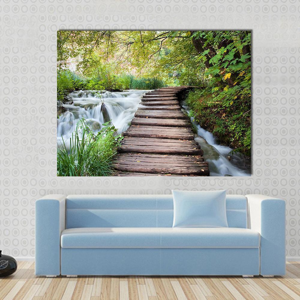 Wooden Path Along a Forest Stream Canvas Wall Art in white, brown and green, single panel hung on a wall