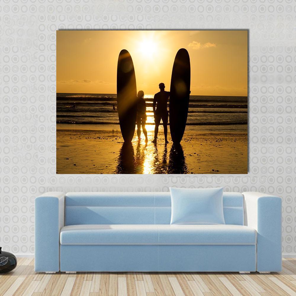 Surfer Couple with Longboards at Sunset Canvas Wall Art in black, orange and yellow, single panel hung on a wall