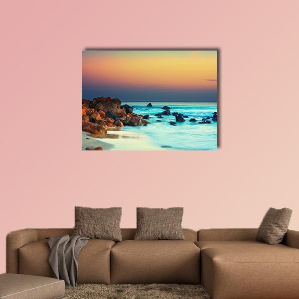 Sunset Over Turquoise Sea with Rocky Shore Canvas Wall Art in orange, yellow and blue, single panel hung on a wall