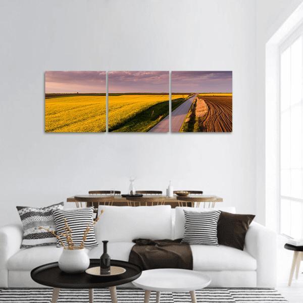 Canola Field Road at Sunset Panoramic Canvas Wall Art in brown, yellow and purple, hung on a wall