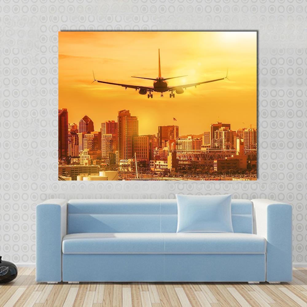 Sunset Airplane Approaching City Skyline Canvas Wall Art in orange and yellow, single panel hung on a wall
