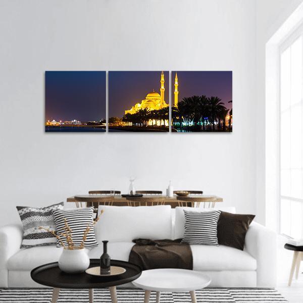 Al Noor Mosque Night Reflection Panoramic Canvas Wall Art in black, yellow and blue, hung on a wall