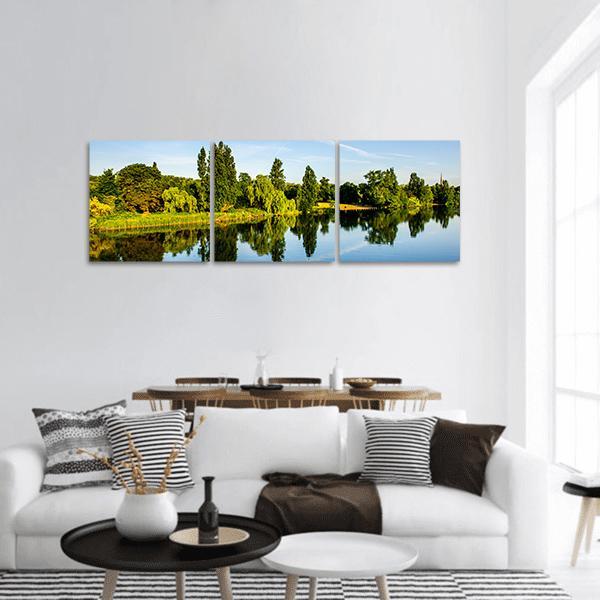 Forest Near Lake with Reflective Water Panoramic Canvas Wall Art in green and blue, hung on a wall