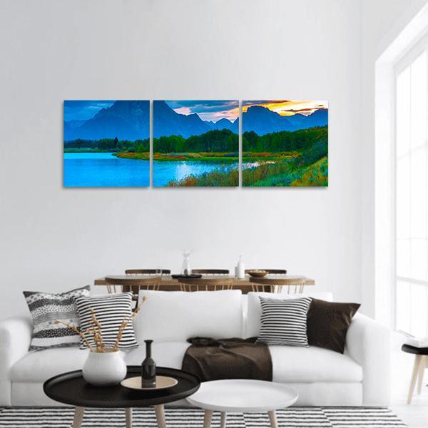 Sunset Over Mountain Lake with Forest Reflection Panoramic Canvas Wall Art in orange, green and blue, hung on a wall