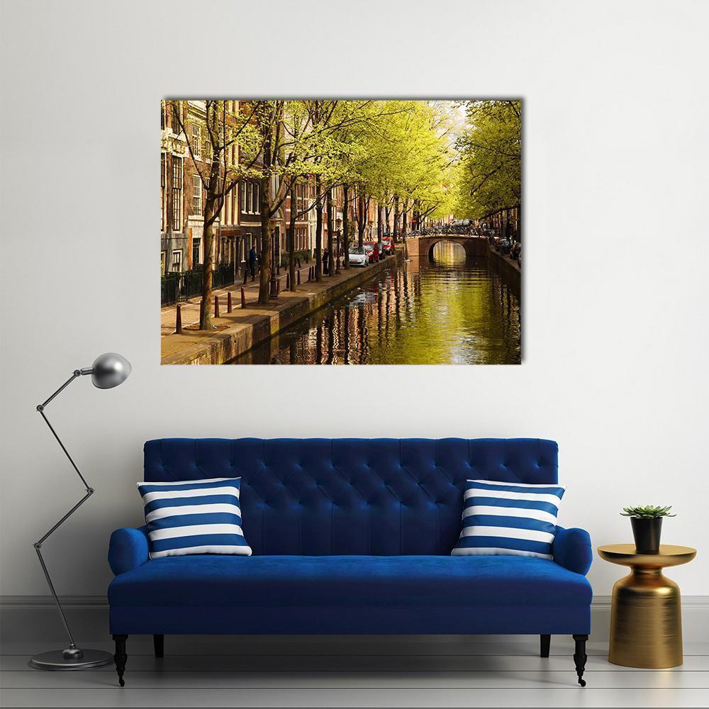 Amsterdam Canal with Blooming Trees Canvas Wall Art in brown, yellow and green, single panel hung on a wall