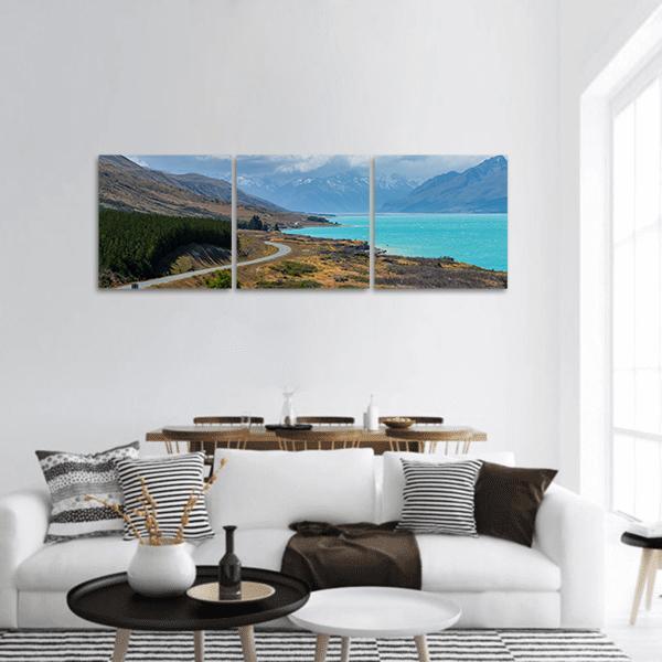 Winding Asphalt Road Along Turquoise Lake Panoramic Canvas Wall Art in gray, brown and blue, hung on a wall