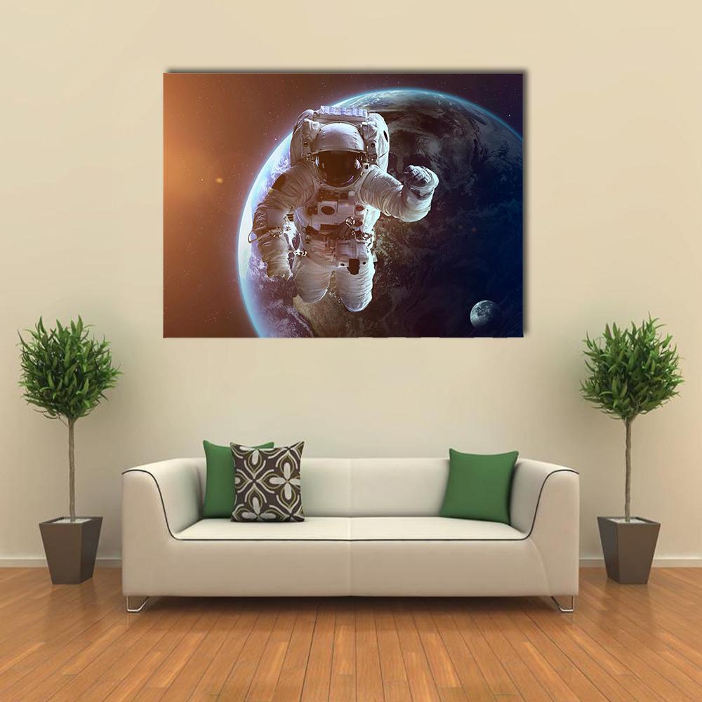 Astronaut Near Planet Earth Canvas Wall Art in black, orange and blue, single panel hung on a wall