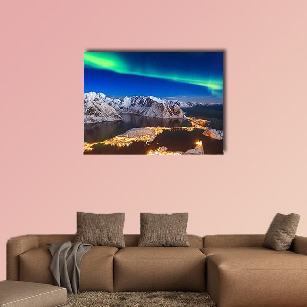 Aurora Over Snowy Mountain Village Canvas Wall Art in white, green and blue, hung on a wall