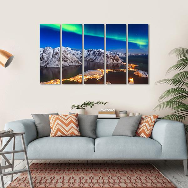 Aurora Over Snowy Mountain Village Canvas Wall Art in white, green and blue, hung on a wall