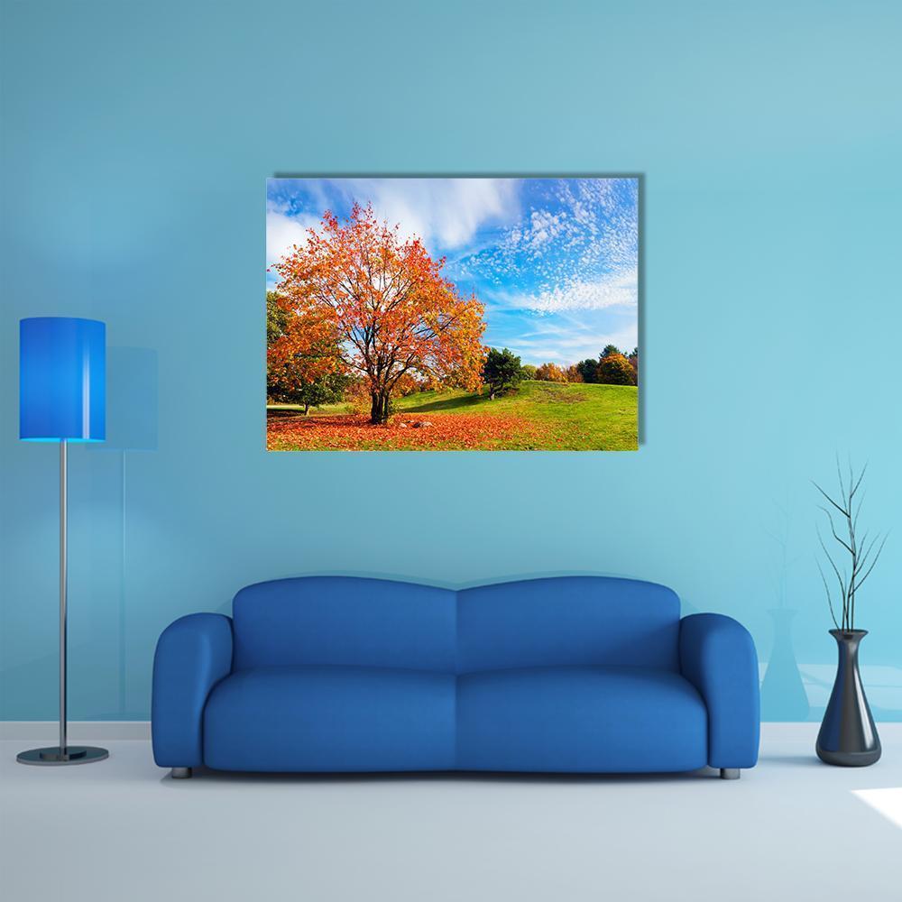 Autumn Tree on Grassy Hill Canvas Wall Art in orange, green and blue, single panel hung on a wall