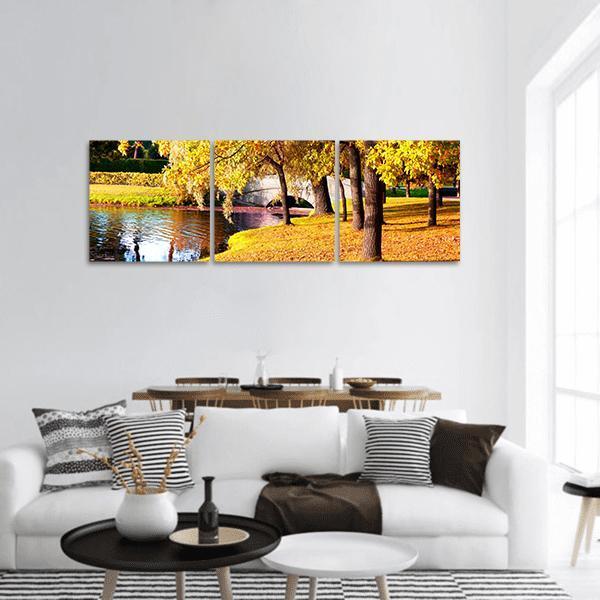 Autumn River with Stone Arch Bridge Panoramic Canvas Wall Art in brown, yellow and green, hung on a wall