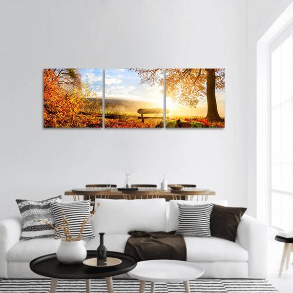 Autumn Sunrise with Lone Bench Panoramic Canvas Wall Art in brown, orange and yellow, hung on a wall