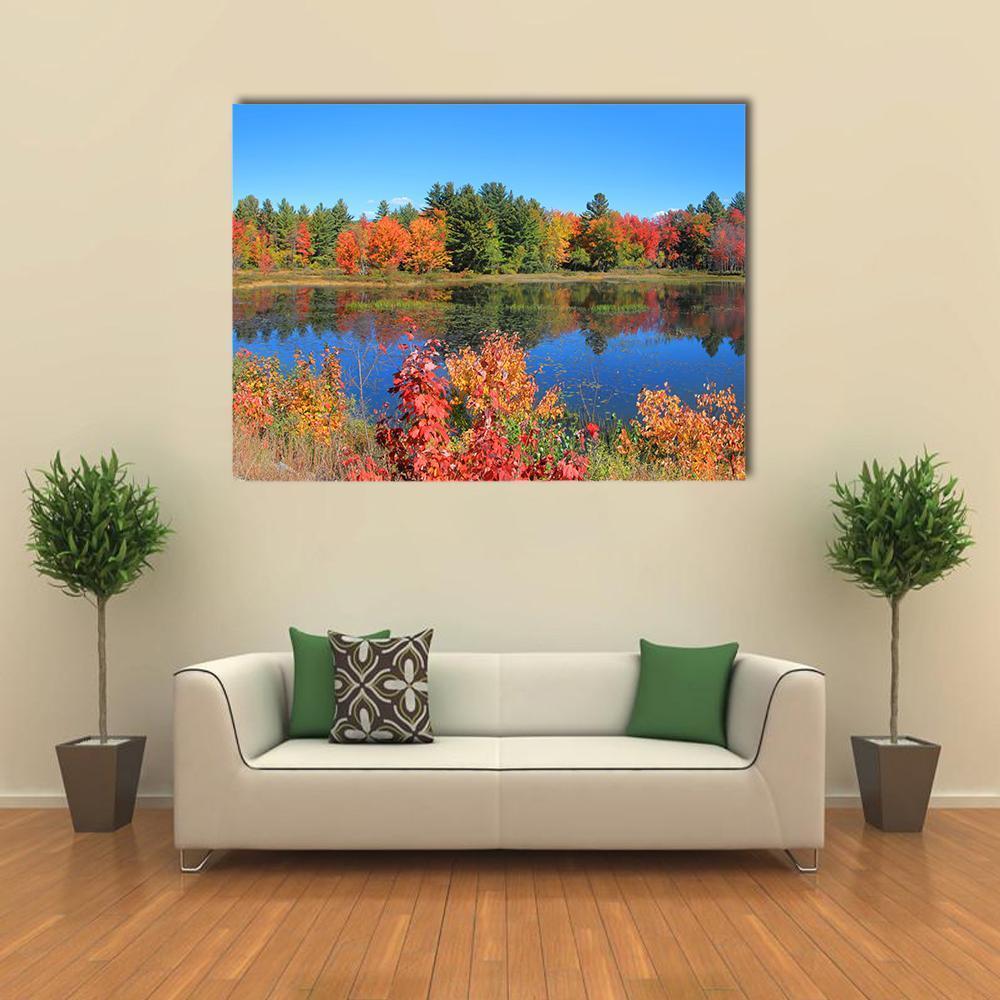 Autumn Trees Reflected in Pond Canvas Wall Art in red, orange and blue, single panel hung on a wall