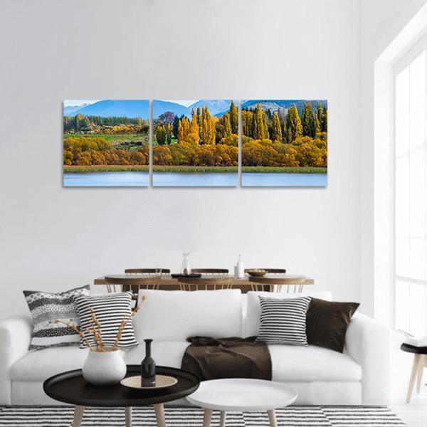 Autumn Lake with Golden Trees Panoramic Canvas Wall Art in orange, yellow and blue, hung on a wall