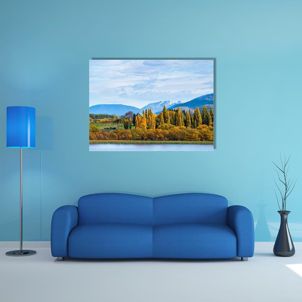 Autumn Trees by the Lake Canvas Wall Art in orange, yellow and blue, single panel hung on a wall