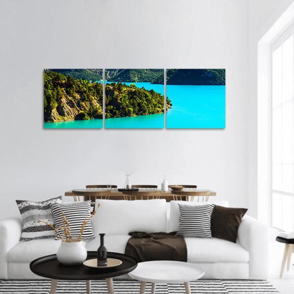 Turquoise Lake with Forested Peninsula Panoramic Canvas Wall Art in green and blue, hung on a wall