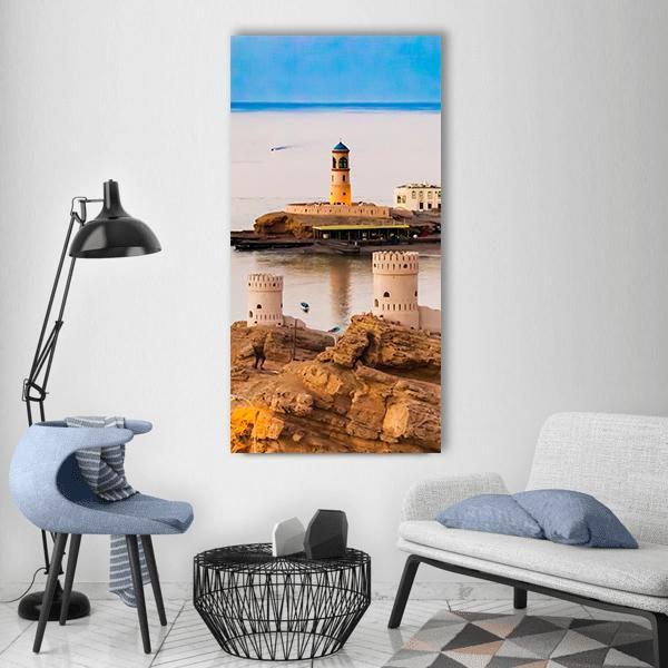 Oman Coastline Lighthouse and Stone Watchtowers Vertical Canvas Wall Art in beige, brown and blue, single vertical panel hung on a wall