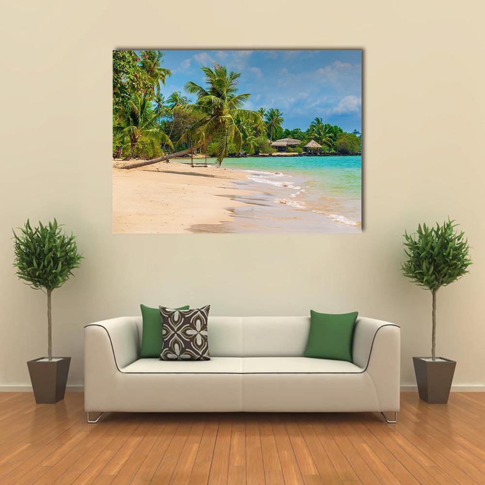 Tropical Beach with Palm Trees and Bungalows Canvas Wall Art in beige, green and blue, single panel hung on a wall