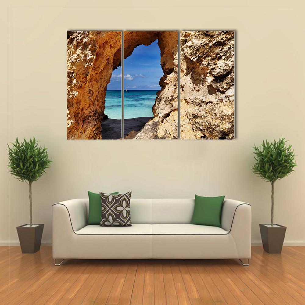 Beach View Through Rock Arch Canvas Wall Art in beige, brown and blue, 3 panel horizontal set hung on a wall