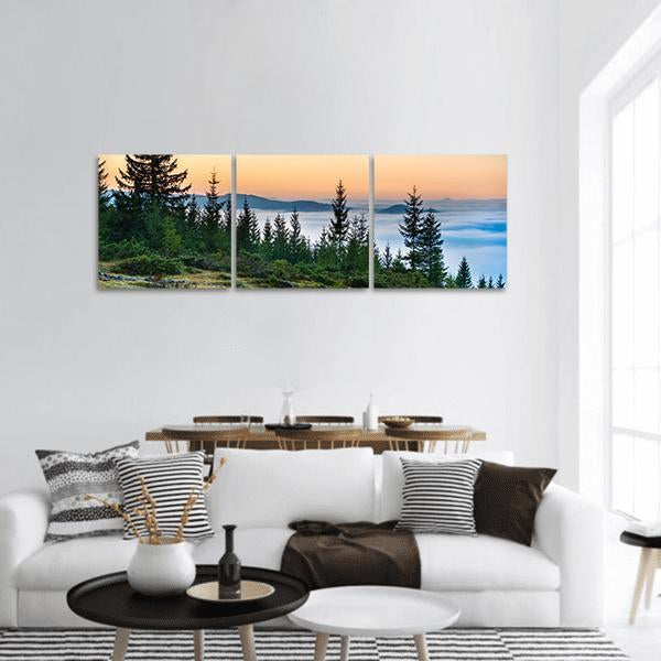 Dawn Forest Above a Sea of Clouds Panoramic Canvas Wall Art in orange, green and blue, hung on a wall