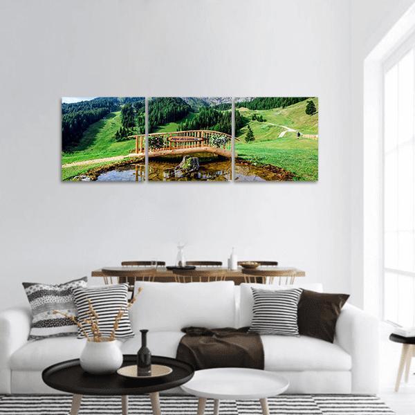 Italian Alpine Park with Wooden Bridge Panoramic Canvas Wall Art in brown, green and blue, hung on a wall