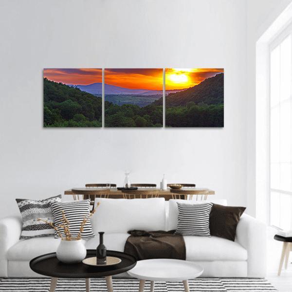 Sunset Over Forested Mountain Valley Panoramic Canvas Wall Art in orange, yellow and green, hung on a wall
