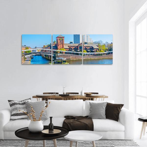 Canal with White Arched Bridge and Clock Tower Panoramic Canvas Wall Art in brown, red and blue, hung on a wall
