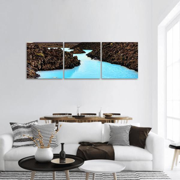 Milky Turquoise Lagoon Among Lava Fields Panoramic Canvas Wall Art in black, brown and blue, hung on a wall