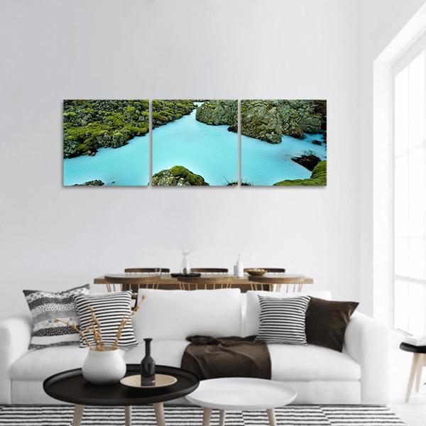 Moss-covered Lava Rocks with Turquoise Pool Panoramic Canvas Wall Art in green and blue, hung on a wall
