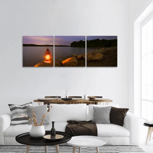 Lantern at Dusk Over Calm Lake Panoramic Canvas Wall Art in brown, orange and purple, hung on a wall