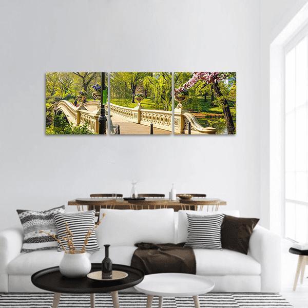 Bow Bridge with Cherry Blossoms Panoramic Canvas Wall Art in beige, green and pink, hung on a wall