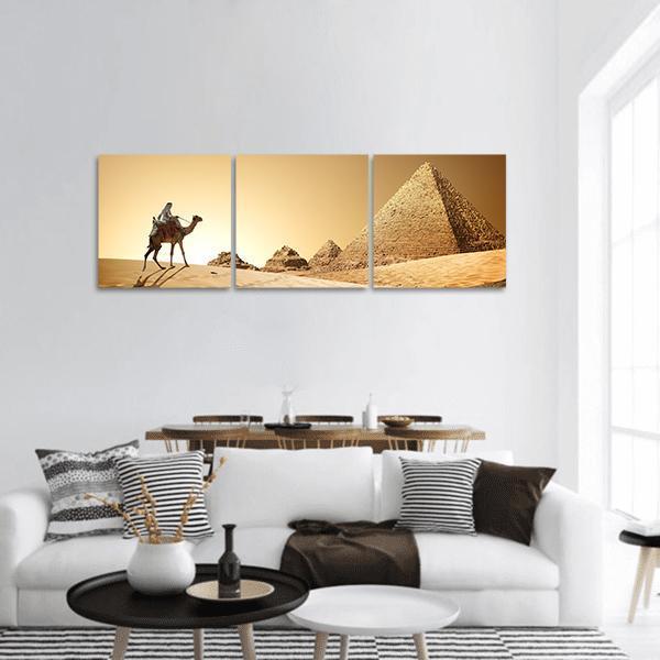 Camel and Pyramids at Golden Hour Panoramic Canvas Wall Art in brown, gold and yellow, hung on a wall