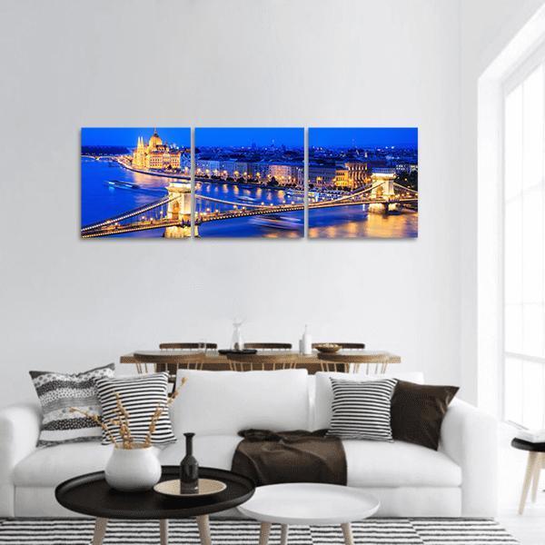 Chain Bridge and Hungarian Parliament at Night Panoramic Canvas Wall Art in gold, yellow and blue, hung on a wall