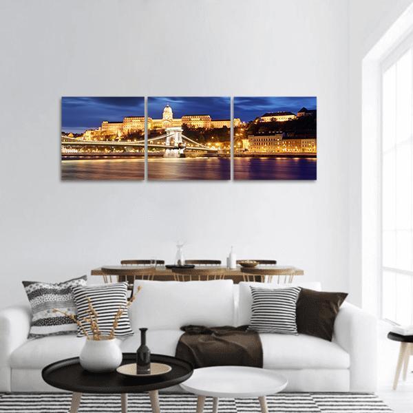 Budapest Chain Bridge at Night Panoramic Canvas Wall Art in gold, yellow and blue, hung on a wall