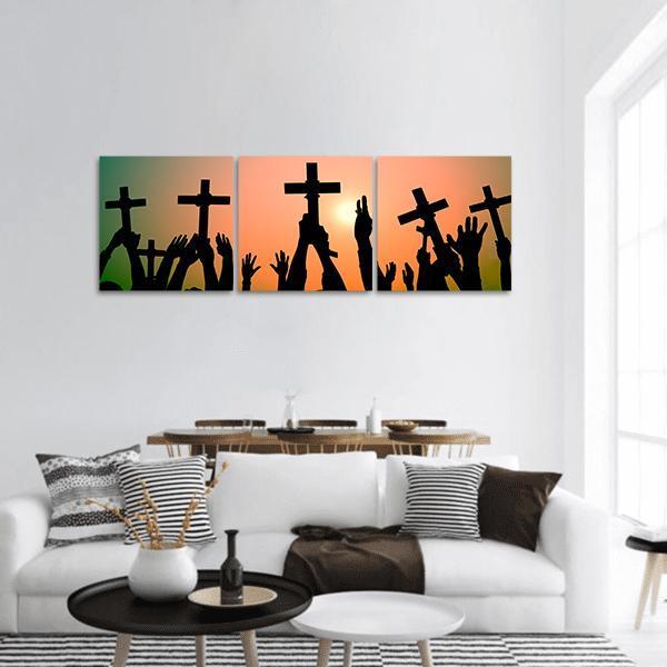 Hands Holding Crosses at Sunset Panoramic Canvas Wall Art in black, orange and yellow, hung on a wall