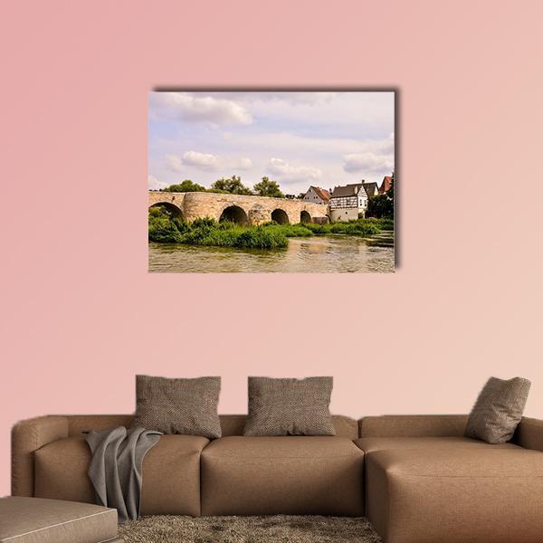 Classic European Village with Stone Arch Bridge Canvas Wall Art in beige, green and blue, single panel hung on a wall