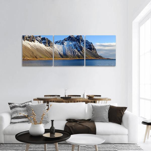 Snow-dusted Cliff Beside Lake Panoramic Canvas Wall Art in white, brown and blue, hung on a wall