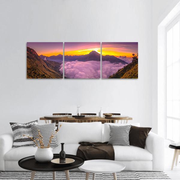 Sunset Over Cloud-filled Mountain Valley Panoramic Canvas Wall Art in orange, yellow and purple, hung on a wall